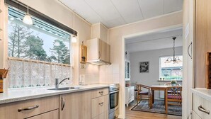 A modern kitchen with wooden cabinets, a stainless steel sink, and a dining area with a wooden table and chairs. - 5 Person Holiday Home in Skjern (Skjern)