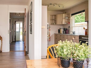 A kitchen with wooden cabinets, a microwave, and a stove. There is a window with a view of greenery outside. - 5 Person Holiday Home in Skjern (Skjern)
