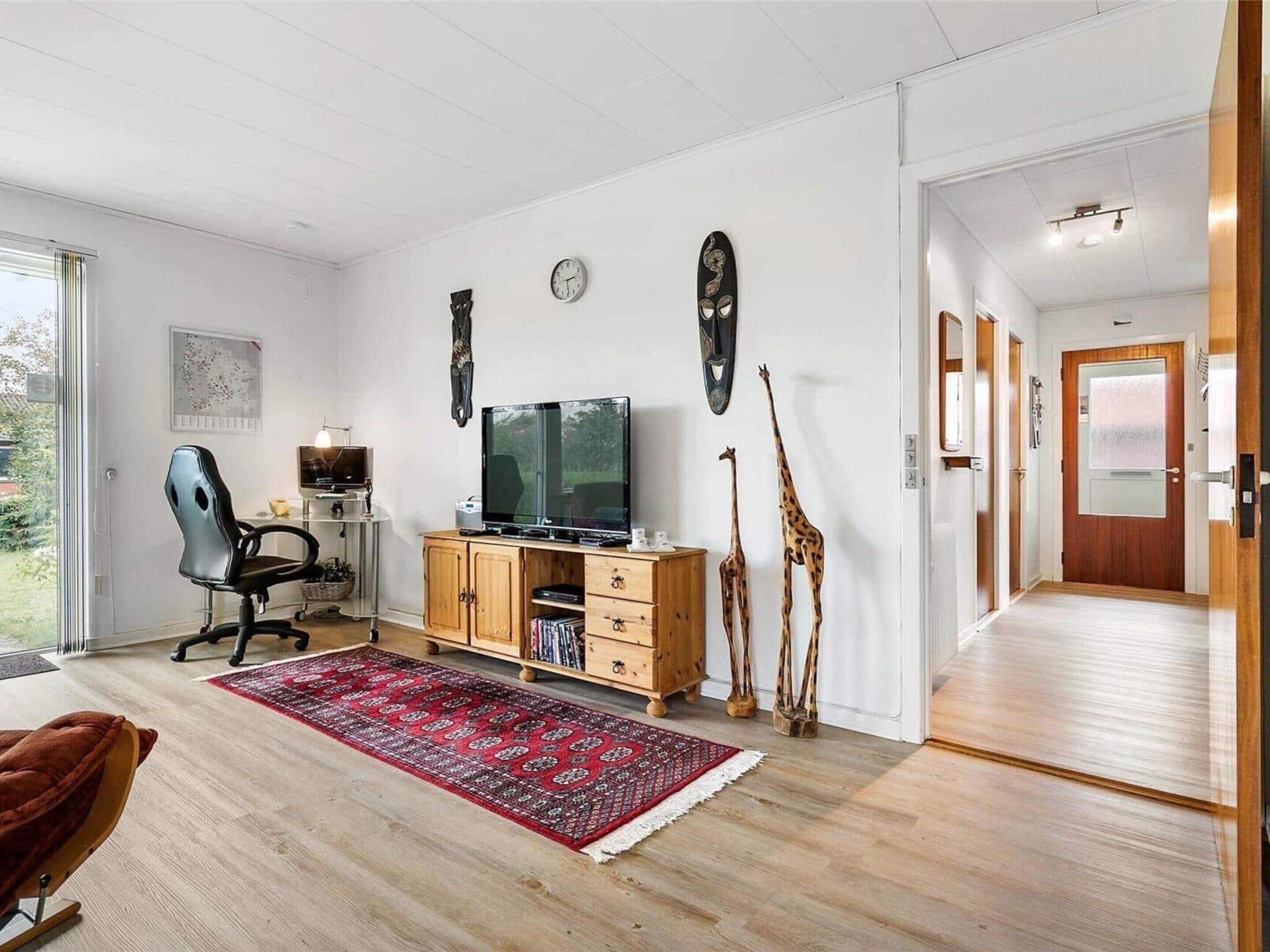 A modern living room with a large flat-screen TV, wooden cabinets, a red patterned rug, and two giraffe sculptures.
