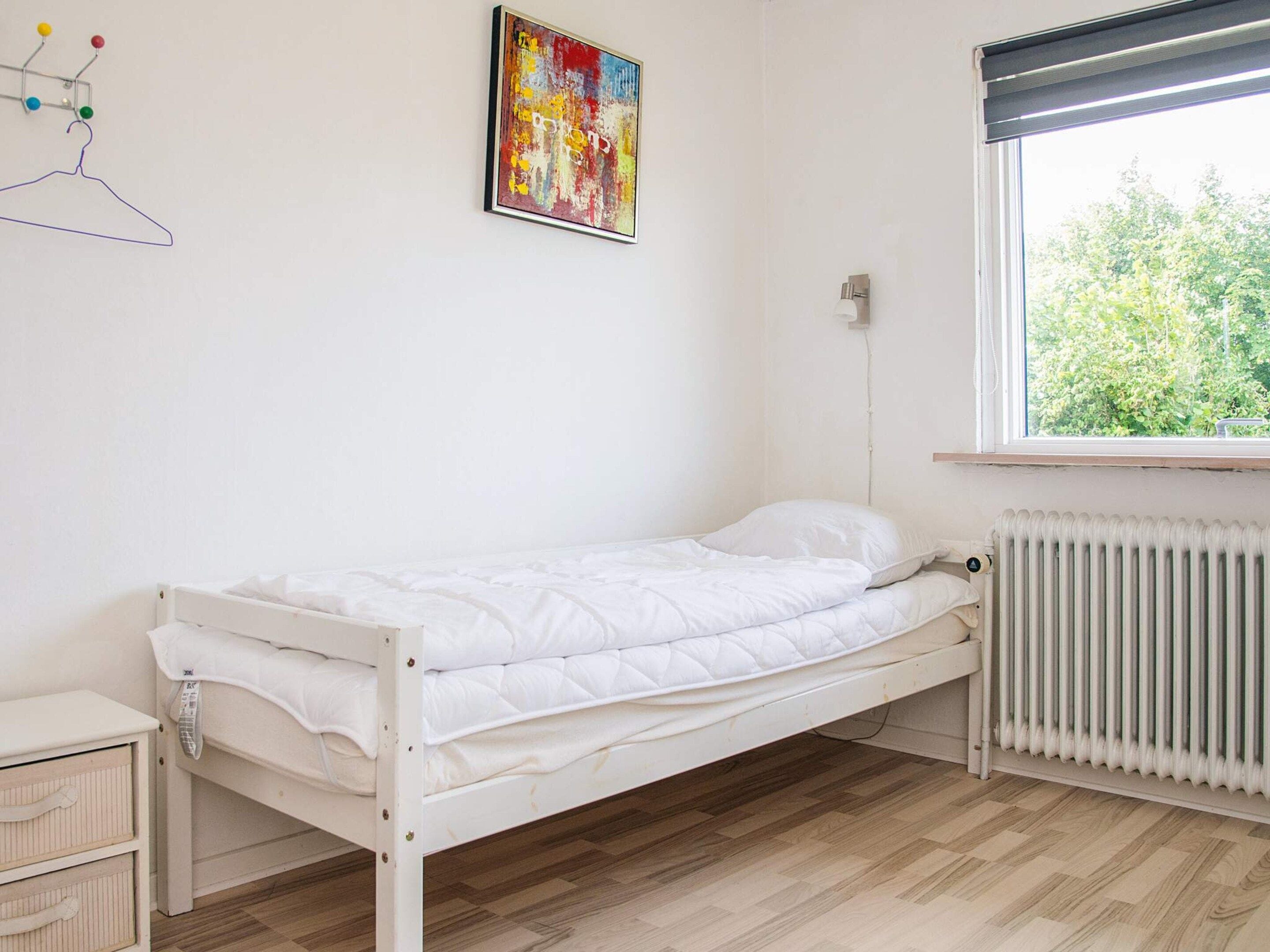 Yhden hengen huone, jossa on valkoinen sänky, patteri, ikkuna, josta on näkymä vehreään maisemaan, ja värikäs abstrakti maalaus seinällä.