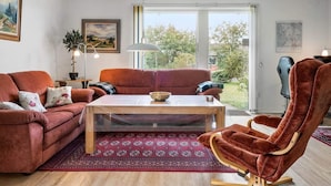 A living room with a sofa, a chair, a coffee table, and a view through a glass door. - 5 Person Holiday Home in Skjern (Skjern)
