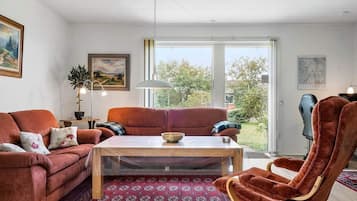 Uma sala de estar com sofá, uma poltrona, mesa de centro e vista através de uma porta de vidro.