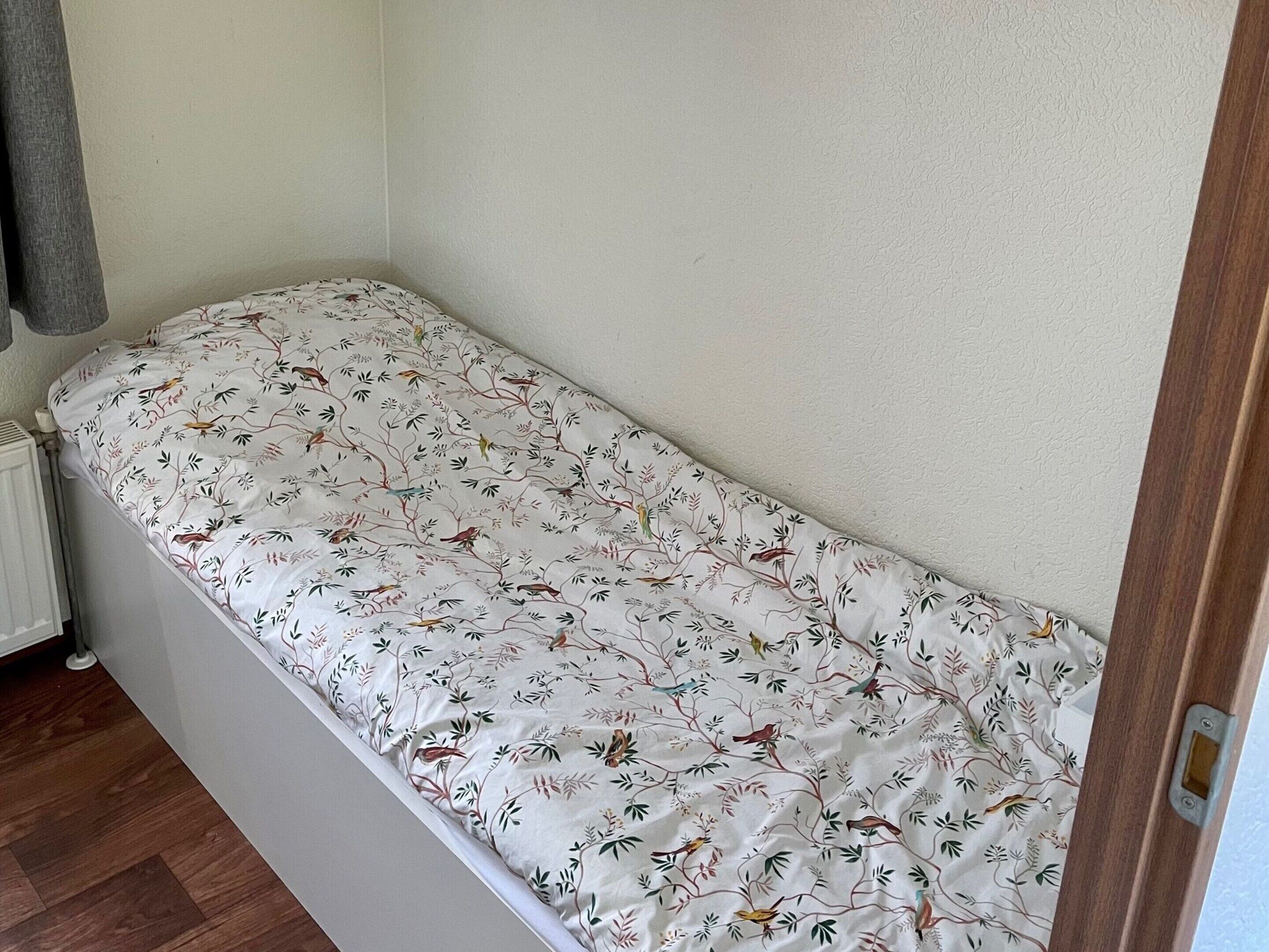 A small, single-bed room with a floral-patterned bedspread, a radiator, and wooden flooring.