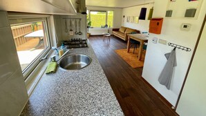 A kitchen with a sink, stove, and wooden flooring. There is a window with a view of a wooden deck.