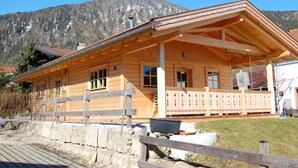 A wooden cabin with a balcony, a stone foundation, and a mountainous backdrop. - Fantastic Apartment in Schleching (Schleching)
