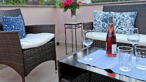 A rooftop terrace with wicker furniture, a table with wine glasses and a bottle, and a view of a hillside with buildings. - Casa Oreggi Comfortable Holiday Residence (Prela)