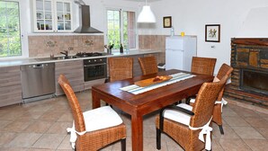 A modern kitchen with a dining area, featuring a large wooden table, wicker chairs, and a stone fireplace. - Casa Oreggi Comfortable Holiday Residence (Prela)