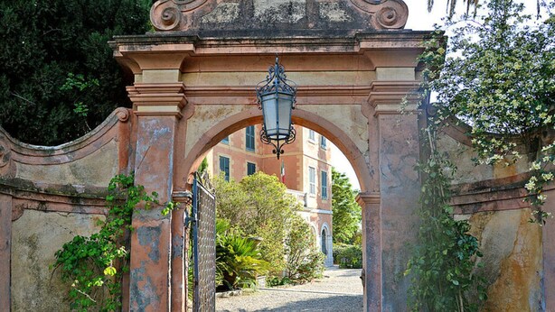 An ornate stone archway with a lantern, leading to a building with a red facade and arched windows. - Casa Oreggi Comfortable Holiday Residence (Prela)