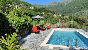 A pool with stone tiles, surrounded by red lounge chairs and a palm plant. - Casa Oreggi Comfortable Holiday Residence (Prela)