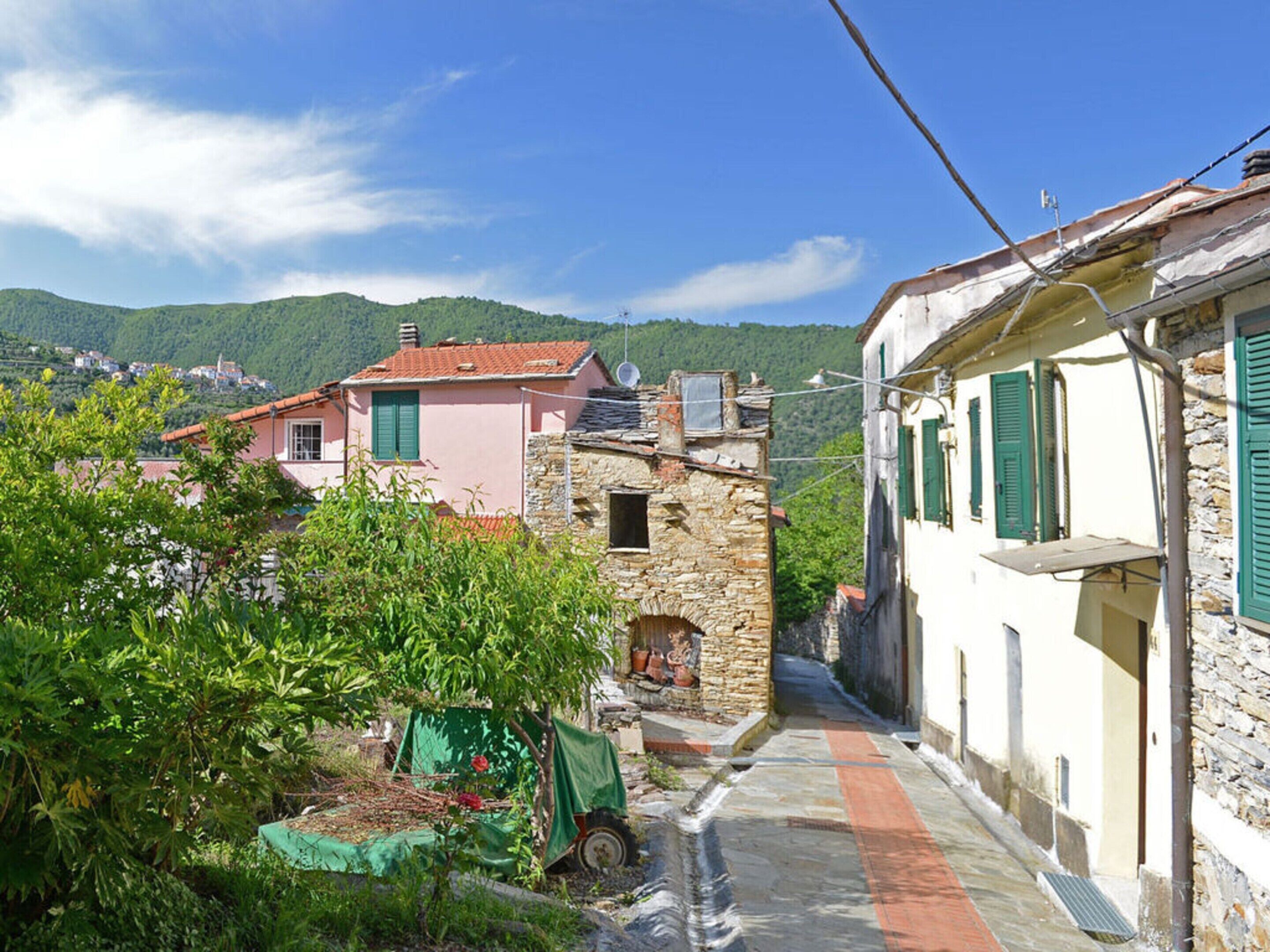 A narrow street with traditional stone buildings, a small garden with a green table, and a clear blue sky.
