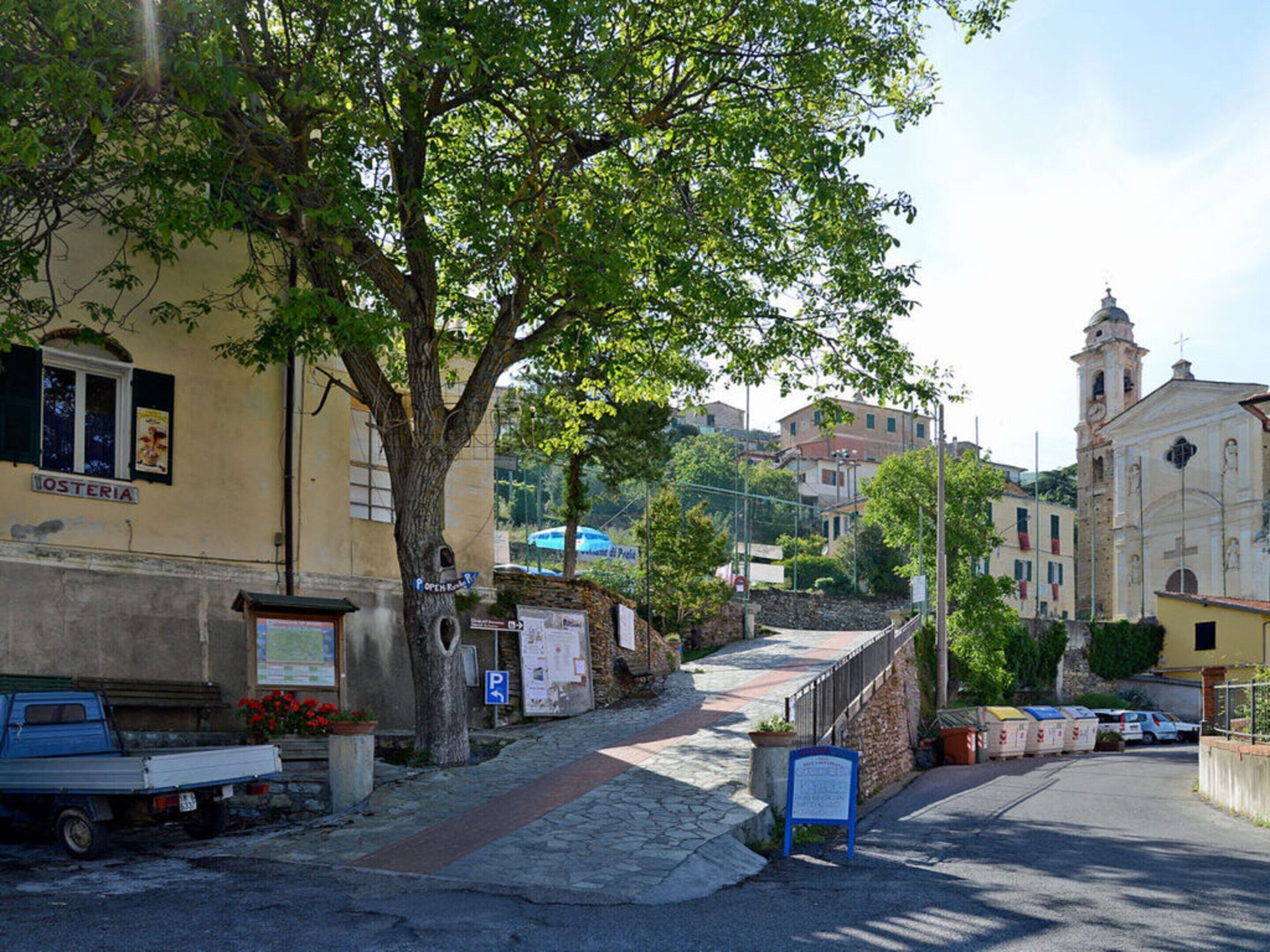 En gatuscen med en byggnad som har skylten "OSTERIA" och en kyrka i bakgrunden.