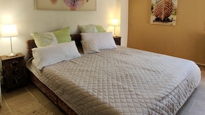 A neatly made bed with a quilted blanket, two bedside tables with lamps, a wall-mounted painting of flowers, and a framed picture of a boat. - Casa Oreggi Comfortable Holiday Residence (Prela)