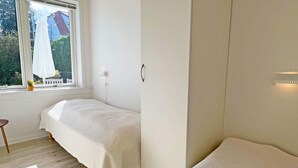 Une chambre avec deux lits simples, une fenêtre donnant sur un espace verdoyant et une petite table près de la fenêtre.