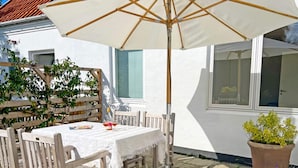 Une terrasse extérieure avec une table dressée pour deux personnes, entourée de chaises en bois, sous un grand parasol.
