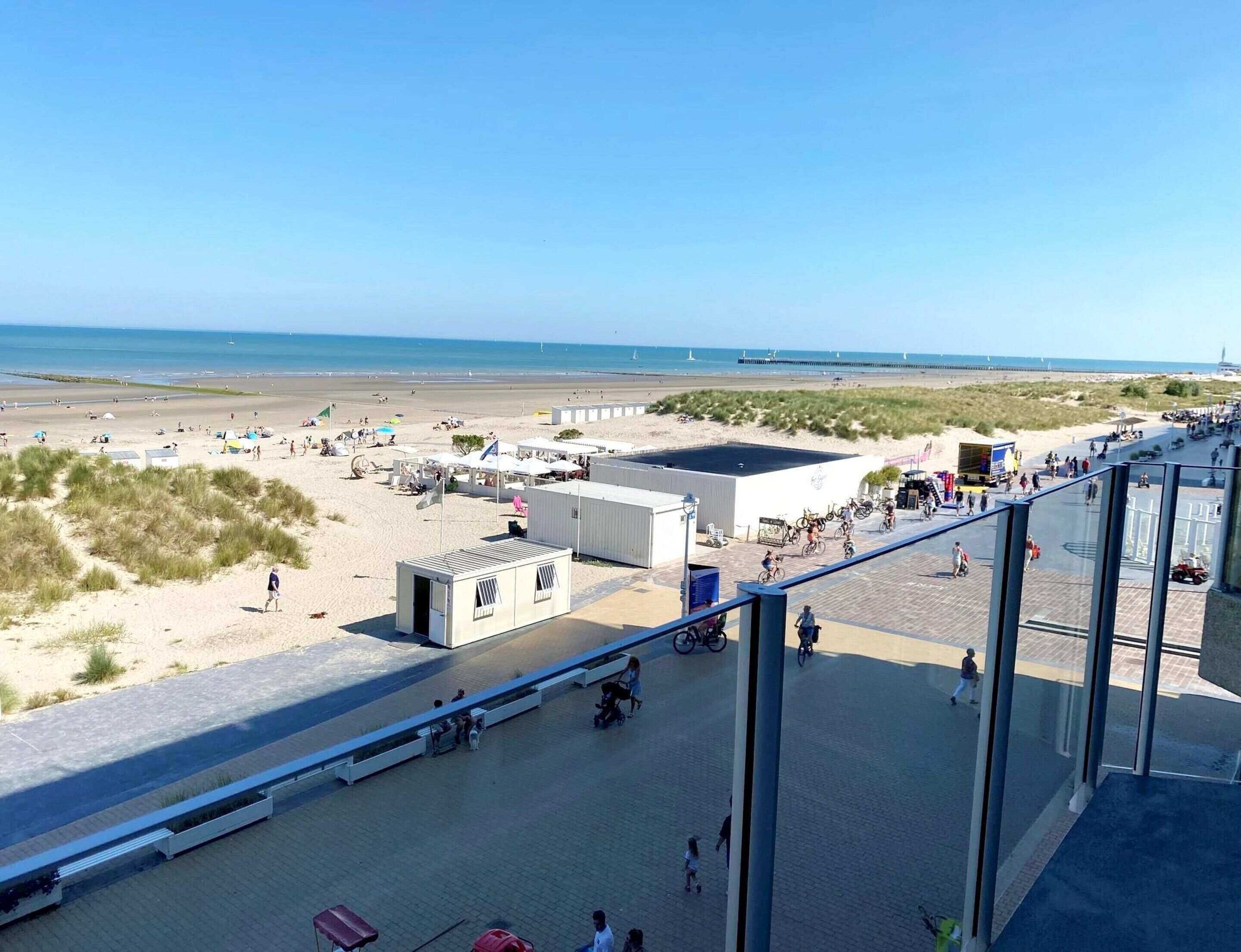 A beachside view with a paved walkway, beach huts, and a clear view of the sea.