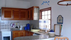 Uma cozinha com armários de madeira, bancada de granito, fogão e janela com cortinas.
