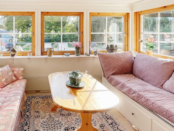 A cozy room with a wooden table, a pink sofa, and a window with a view of greenery.