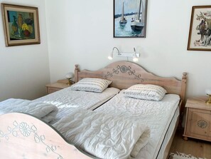 A double bed with a wooden headboard, two bedside tables, and a nightstand with a lamp. There are three framed artworks on the walls.