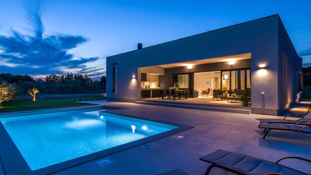 Ein modernes Haus mit Pool, Sitzgelegenheiten im Freien und einer gut beleuchteten Terrasse.