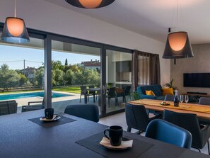 A modern dining area with a pool view, a dining table, chairs, and a sofa. - Villa Polei Comfortable Holiday Residence (Pula)