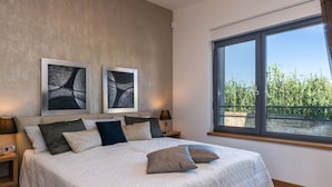 Ein Schlafzimmer mit einem großen Bett, zwei Nachttischen und einem Fenster mit Blick auf Grünflächen.