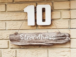 Une enseigne en bois rustique, portant le numéro 10 et l’inscription « Strandhaus », est accrochée à un mur de briques.