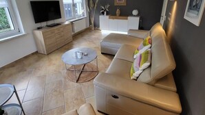 A modern living room with a beige sofa, a TV, a dining table, and a kitchen area. - Lighthouse View Modern Retreat (Bastorf)