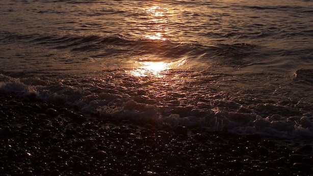A sunset over the ocean with waves reaching the shore. - Lighthouse View Modern Retreat (Bastorf)