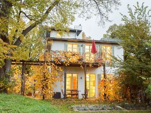 A two-story house with a balcony, surrounded by trees with autumn leaves. - Holiday Apartment on the Upper Floor (Werder (Havel))