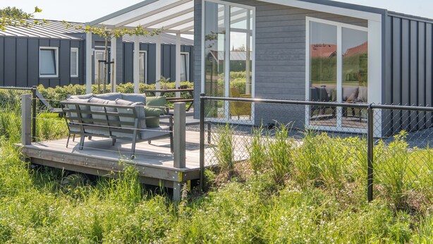 A modern outdoor seating area with a wooden deck and a glass enclosure. - Detached House in Zeeland With Scenic Terrace (Wemeldinge)