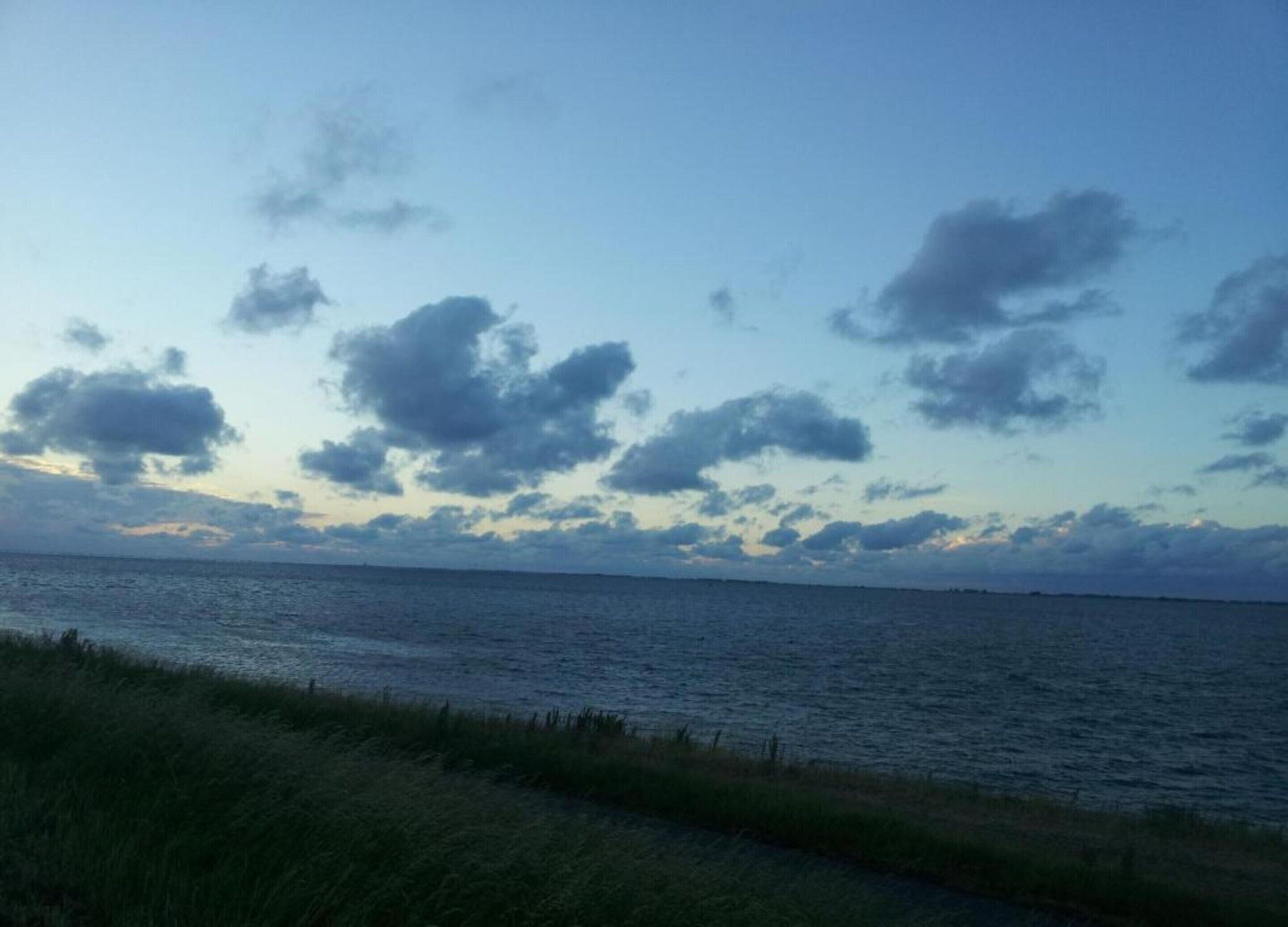 A coastal view with a grassy foreground and a calm sea under a partly cloudy sky.