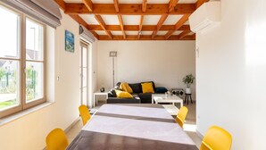 A modern living room with a wooden ceiling, a dining table with yellow chairs, a sofa with yellow cushions, and a small side table with a radio. - Holiday Home in Koksijde Near Sint-andre Beach (Koksijde)