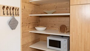 Eine kleine Küche mit Holzschränken, einer weißen Mikrowelle, einer Schüssel und einem Set an Besteck, das an einer Wandhalterung befestigt ist.