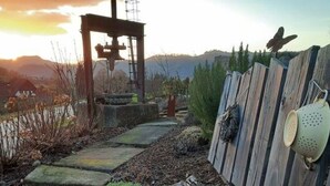 Ein rustikaler Gartenweg mit Holzlattenzaun, Vogelhaus aus Metall und einem großen Wagenrad.