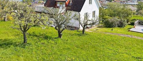 Une maison blanche avec un toit rouge, entourée de verdure et d’arbres, qui surplombe une ville côtière.