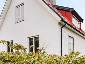 Un bâtiment blanc avec un toit rouge et une gouttière noire. On peut voir deux fenêtres et une porte.
