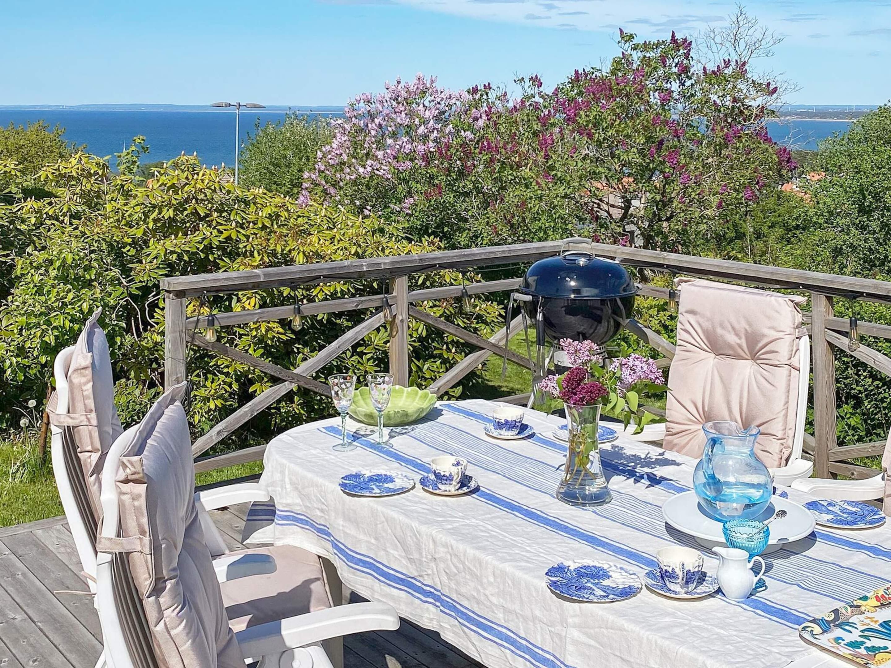 A table set outdoors with a view of the sea, a grill, and a chair.