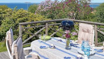A table set outdoors with a view of the sea, a grill, and a chair.