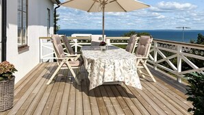 A deck with a table and chairs, a white umbrella, and a view of the sea. - 4 Star Holiday Home in Bastad (Bastad)