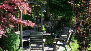 A garden patio with two wooden chairs and a table, surrounded by lush greenery and a pergola structure. - Holiday Home Time out in the Monument (Lohr am Main)