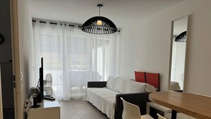 A modern living room with a sofa, a dining table, and a TV. - Très beau T2 3* (office tourisme), grde terrasse, garage proche plage et centre (Cavalaire sur Mer)