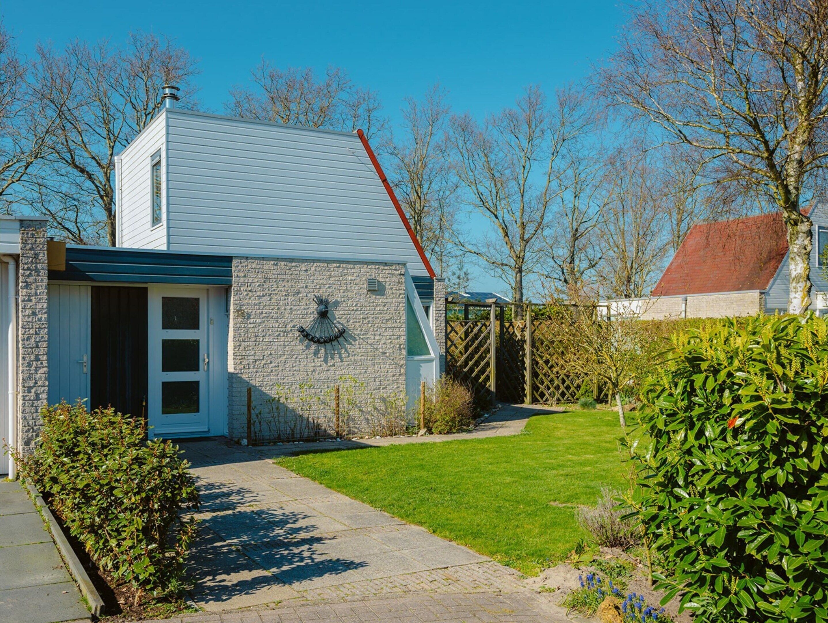 Een huis met een gevel van natuursteen, een blauw dak en een kleine voortuin met gazon en struiken.