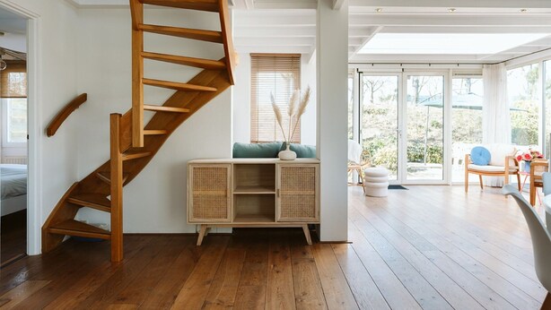 A spacious room with a wooden staircase, a built-in wooden cabinet, and a large sliding glass door leading to an outdoor area. - Holiday Bungalow With a Nice Light Appearance at 1.5 km From the Beach (Ouddorp)