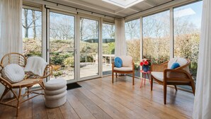 A sunlit room with large sliding glass doors leading to a garden, furnished with wicker chairs and ottomans. - Holiday Bungalow With a Nice Light Appearance at 1.5 km From the Beach (Ouddorp)