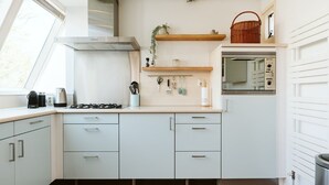 A compact kitchen with white cabinets, a stainless steel range hood, a built-in oven, and a window providing natural light. - Holiday Bungalow With a Nice Light Appearance at 1.5 km From the Beach (Ouddorp)