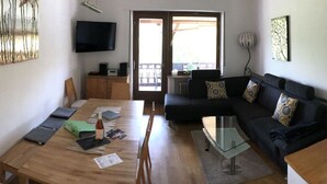 A modern living room with a wooden dining table, a black sofa with patterned cushions, a glass coffee table, and a flat-screen TV mounted on the wall. - Vinum Comfortable Holiday Residence (Uerzig)