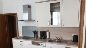 A modern kitchen with white cabinets, a built-in dishwasher, a coffee maker, and a stainless steel sink. - Vinum Comfortable Holiday Residence (Uerzig)