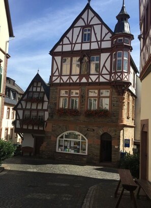 Ein traditionelles Fachwerkhäuschen mit Steinunterbau, einem markanten Turm und einem kleinen Balkon mit Blumen.