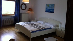 A bedroom with a bed, bedside tables, a lamp, a window with curtains, a radiator, and a painting on the wall. - Vinum Comfortable Holiday Residence (Uerzig)
