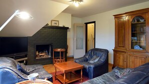Una sala de estar con chimenea, sofá de cuero, aparador de madera y televisor.